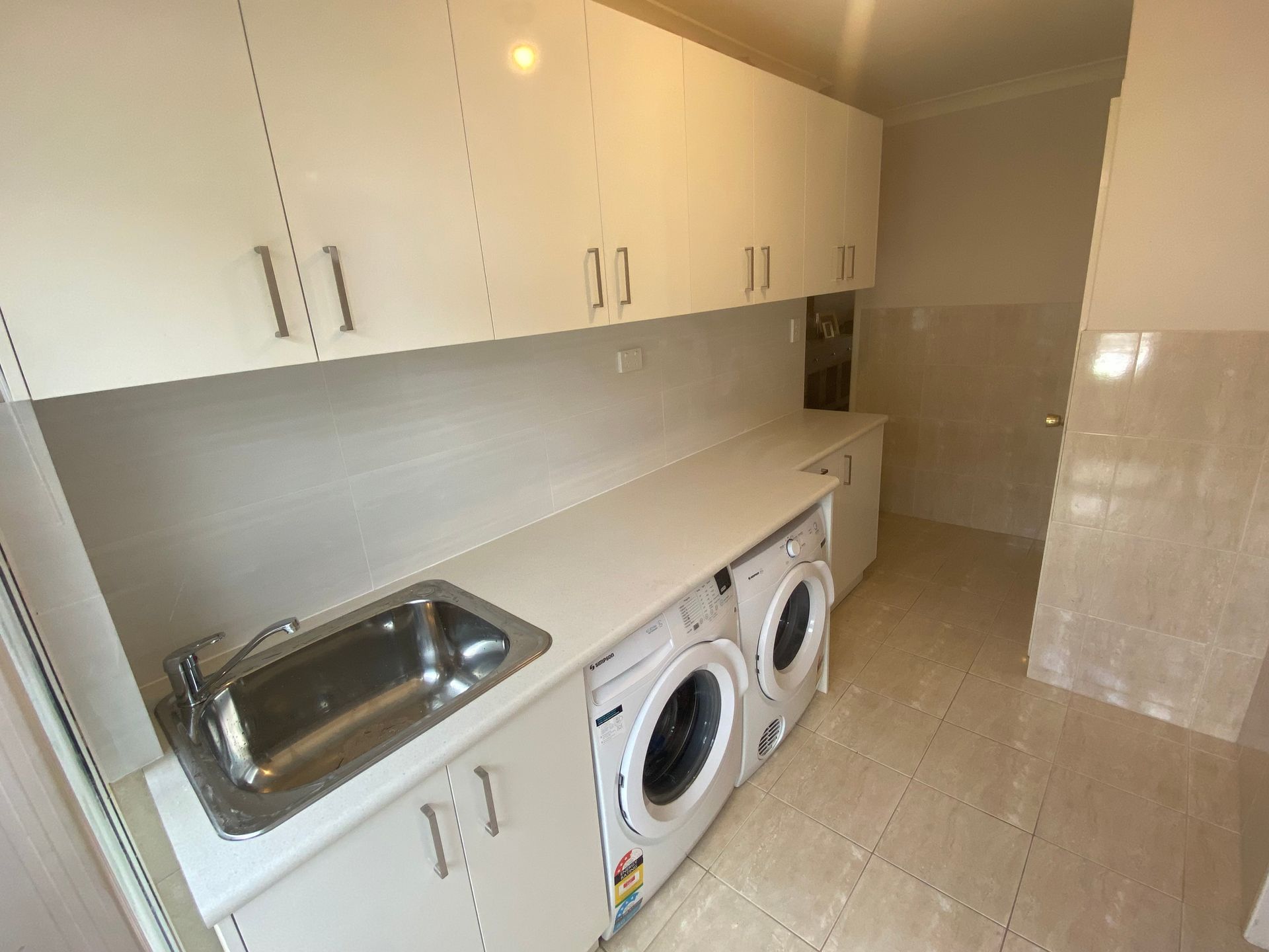 Laundry room with white cabinets, sink, and washing machine.