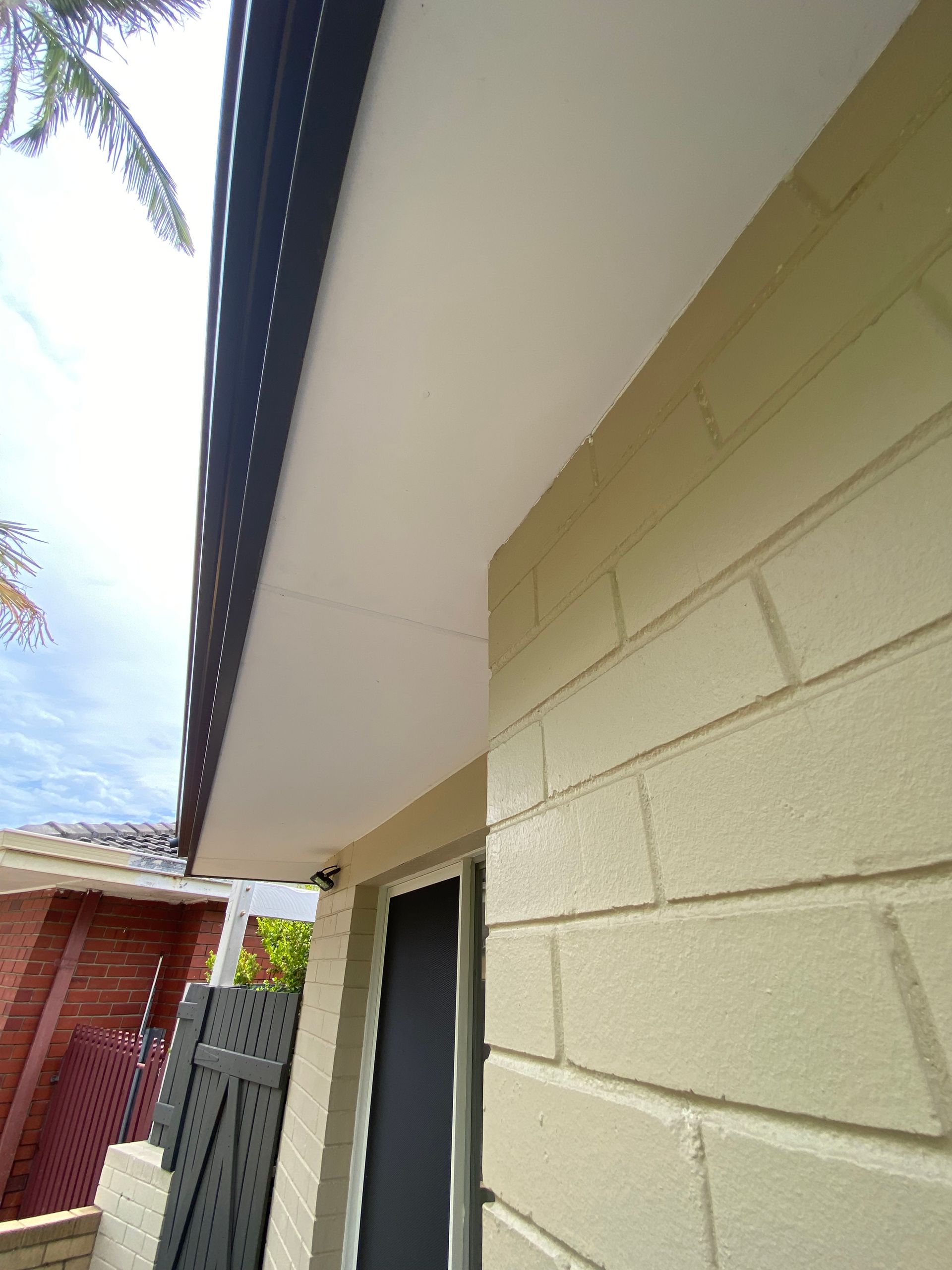 Beige brick building with black trim roof and white underside, against a cloudy sky.