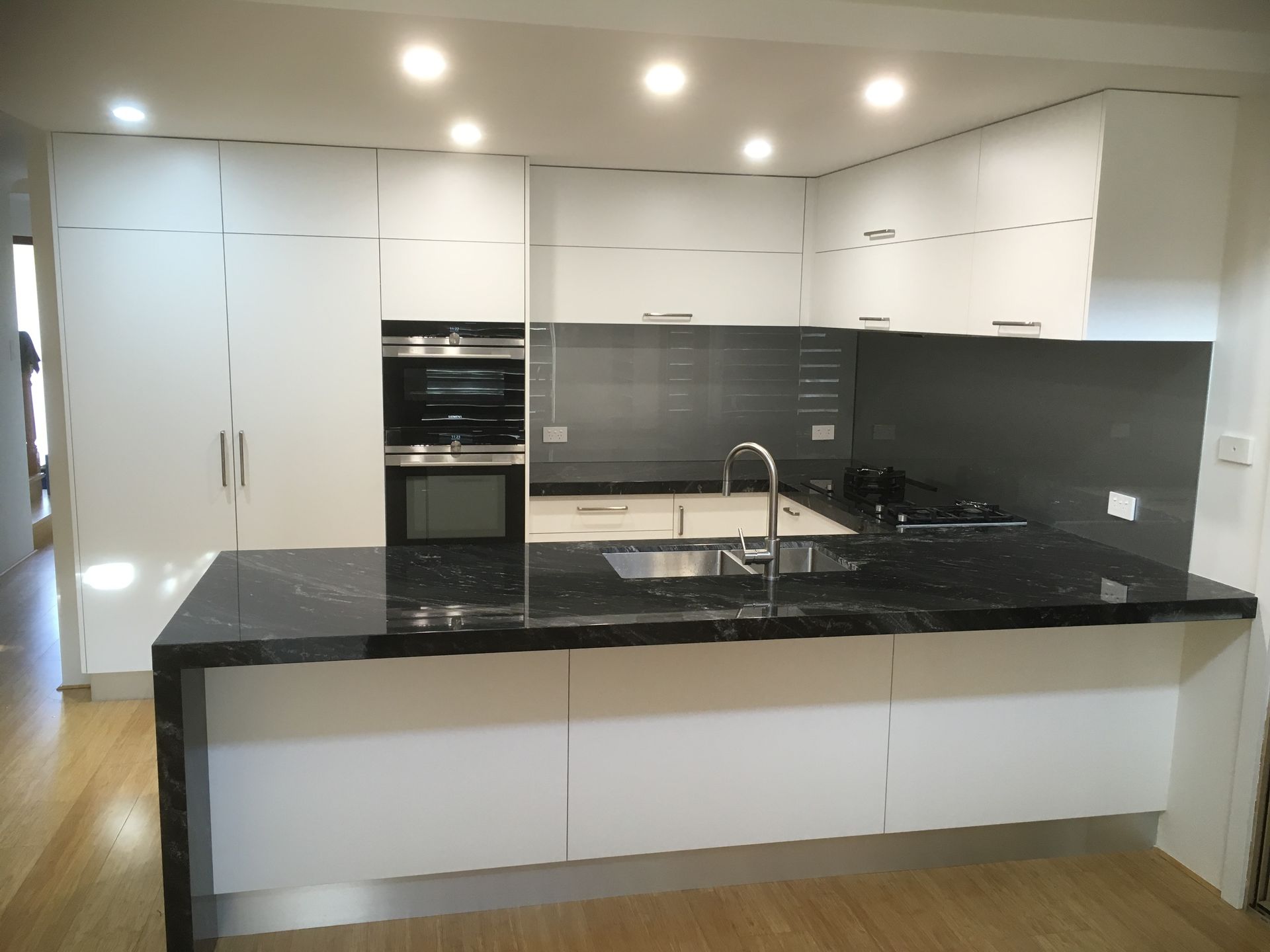 Modern white kitchen with black granite countertop island, stainless steel sink, and gray backsplash.