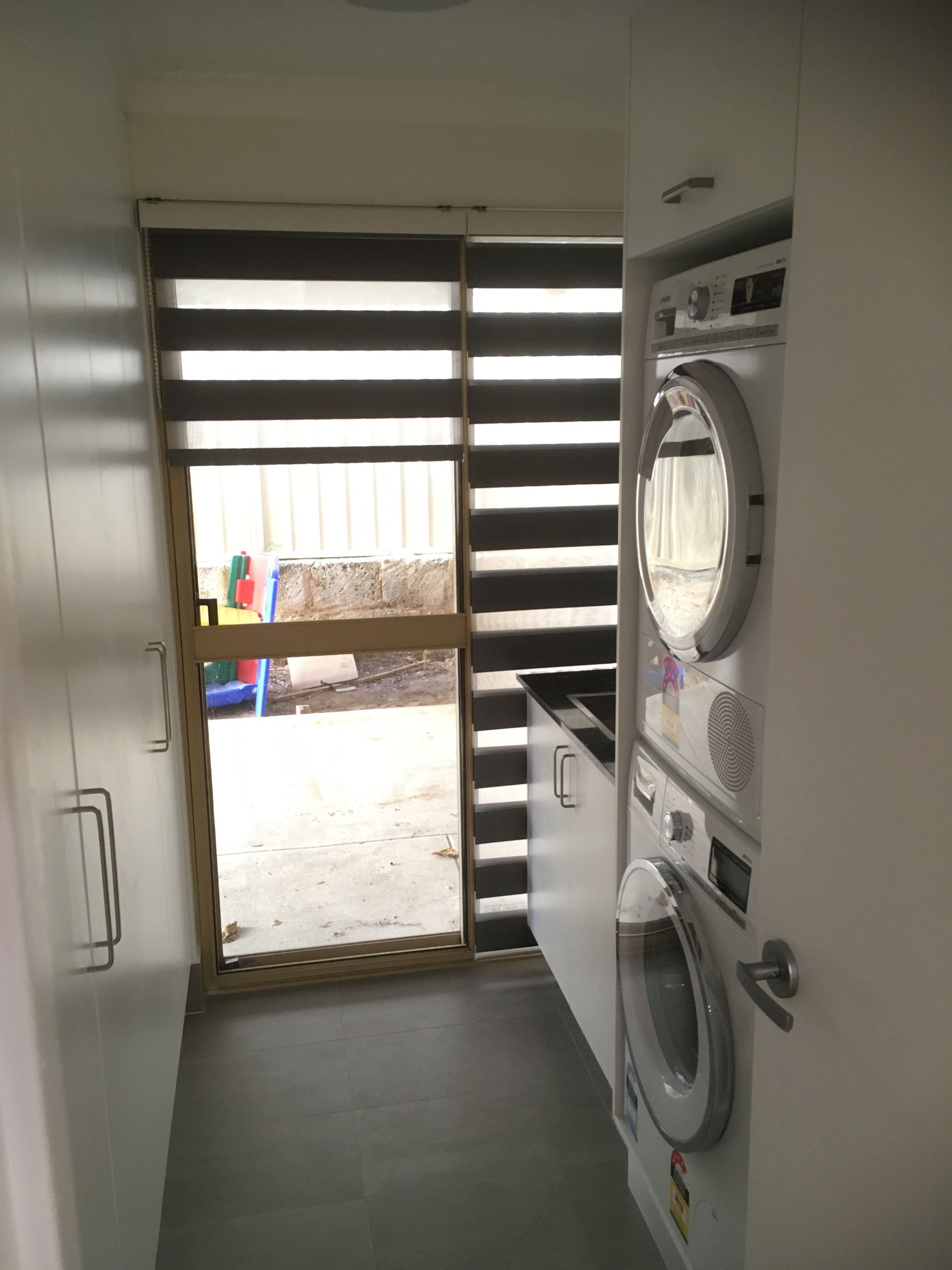 Laundry room with stacked washer/dryer, door to backyard, cabinet.