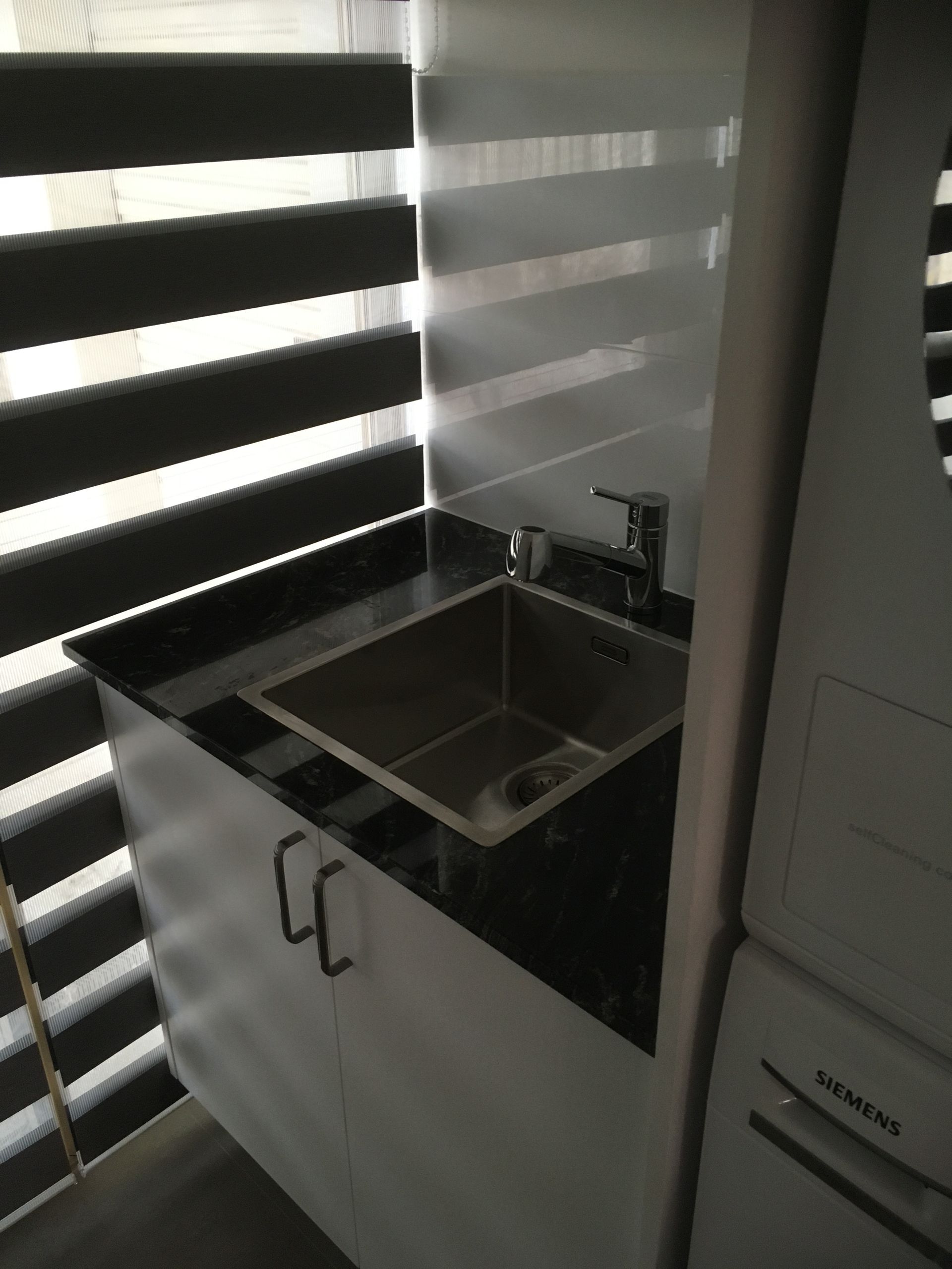 A small sink with a dark granite countertop and white cabinet next to a blind window.