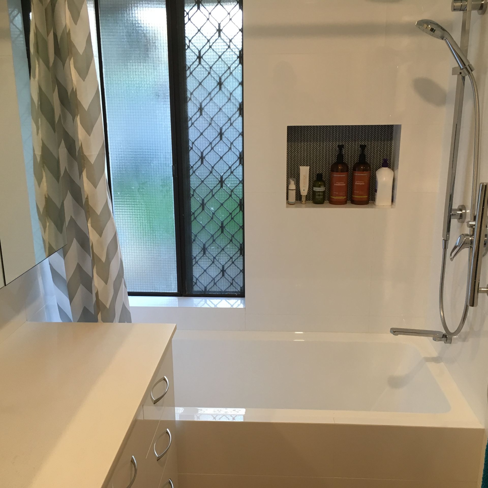 White bathtub with shower, window and shelf holding toiletries.