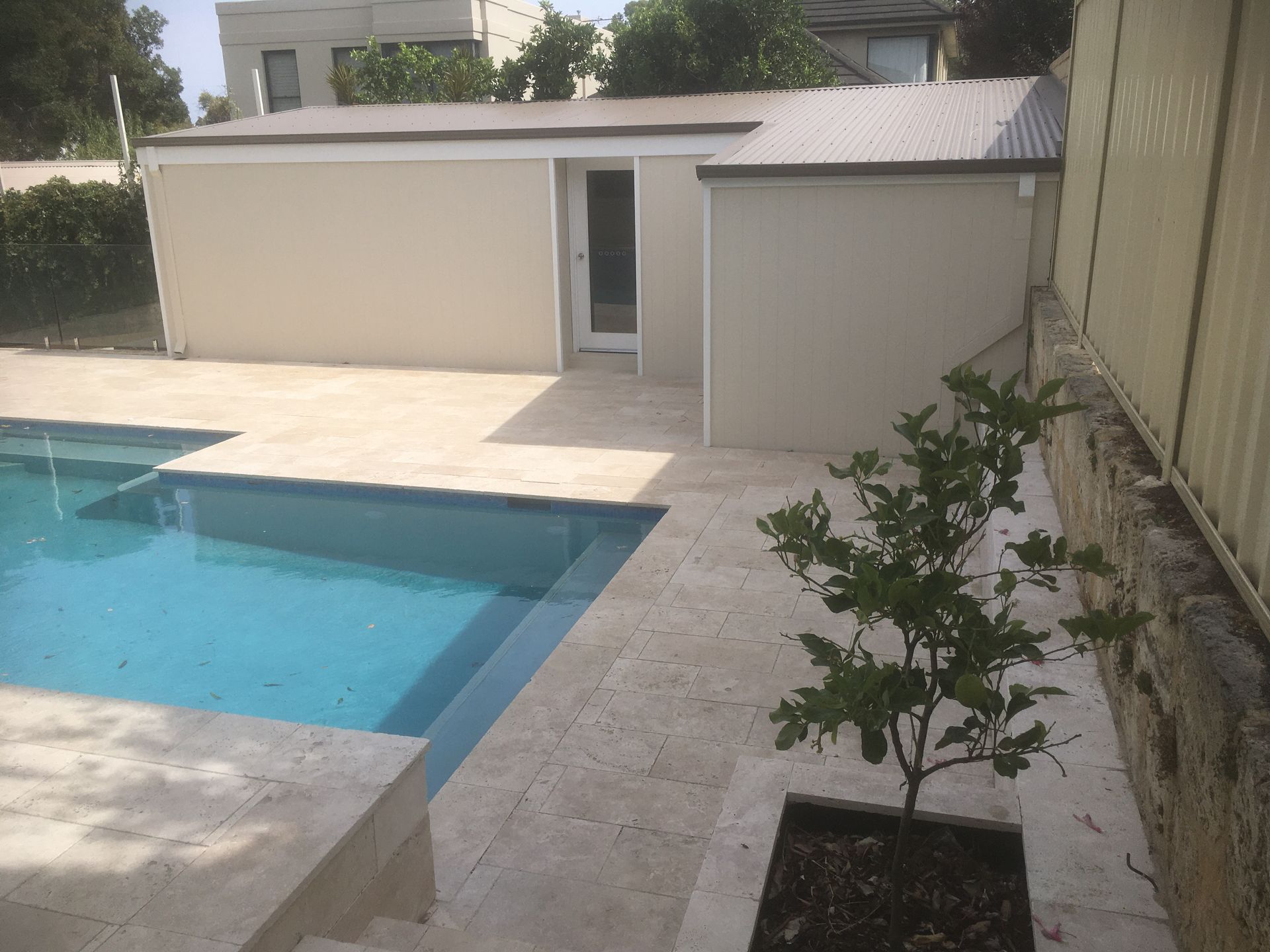 A pool with blue water and a light-colored patio, beige buildings in the background.
