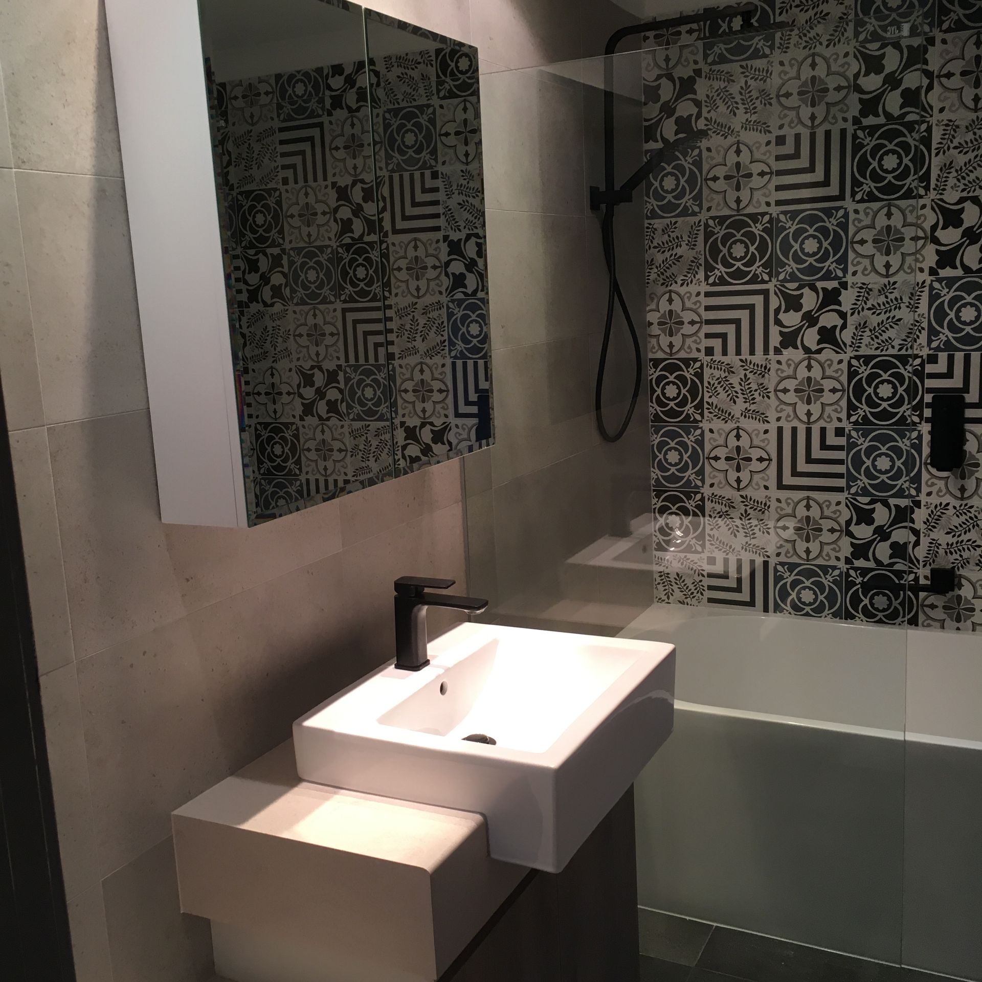 Modern bathroom with white sink, patterned tile, and a black faucet.