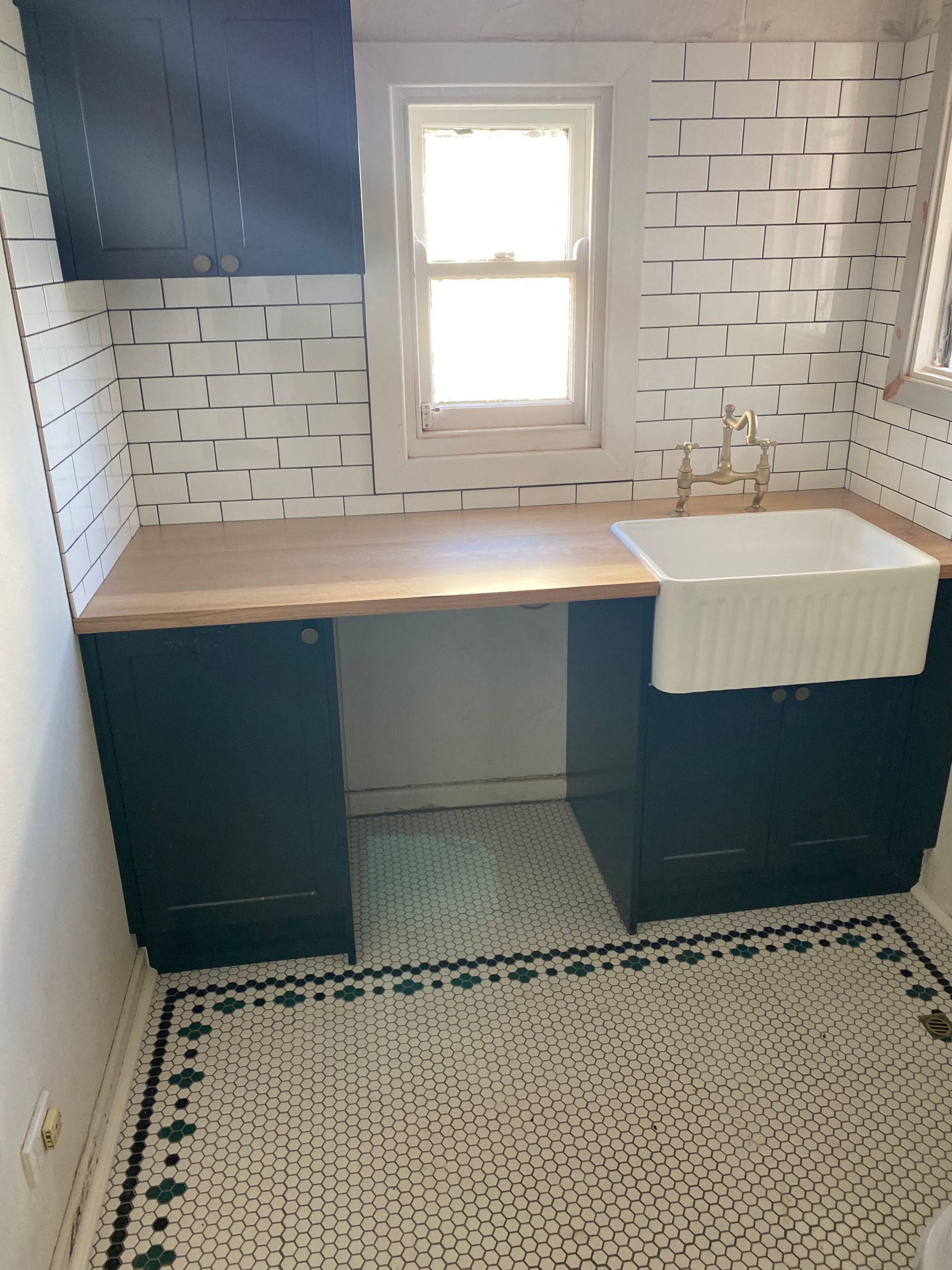 Laundry room with black cabinets, wood countertop, white sink, and patterned tile floor.