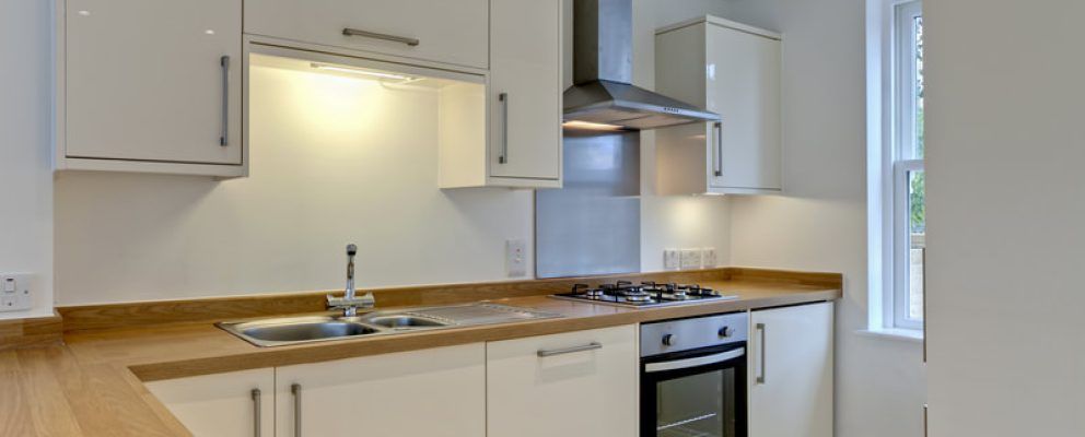 A kitchen with white cabinets , a stove , a sink , and a window.