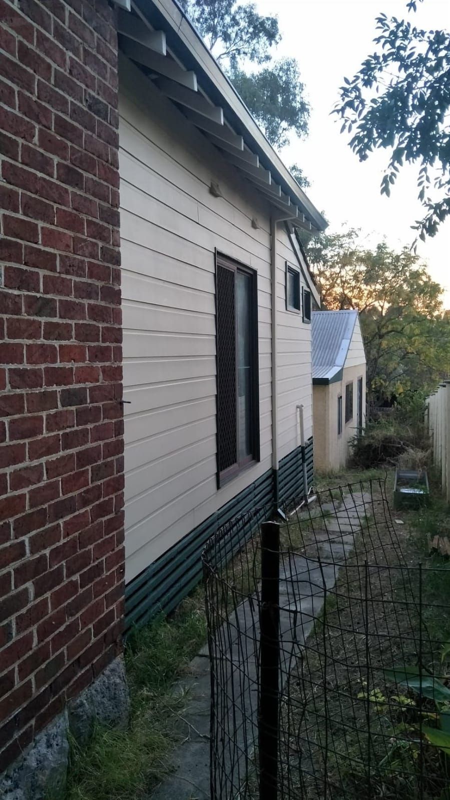A brick building with a white siding and a fence in front of it.