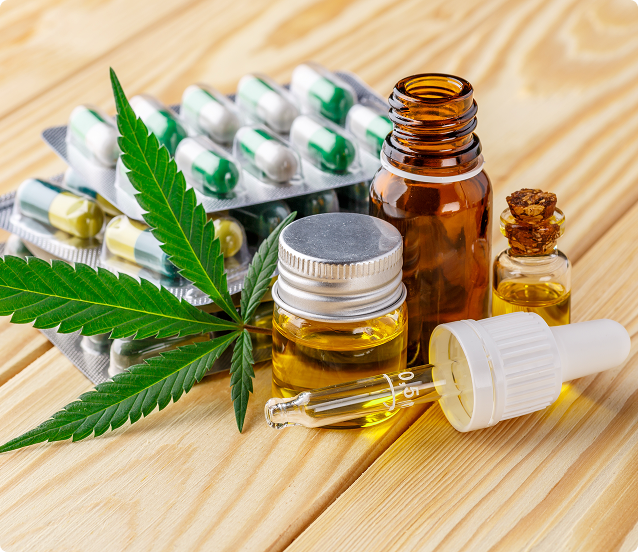 Cannabis leaf, pills, and oil bottles on a wooden surface, suggesting medical use.