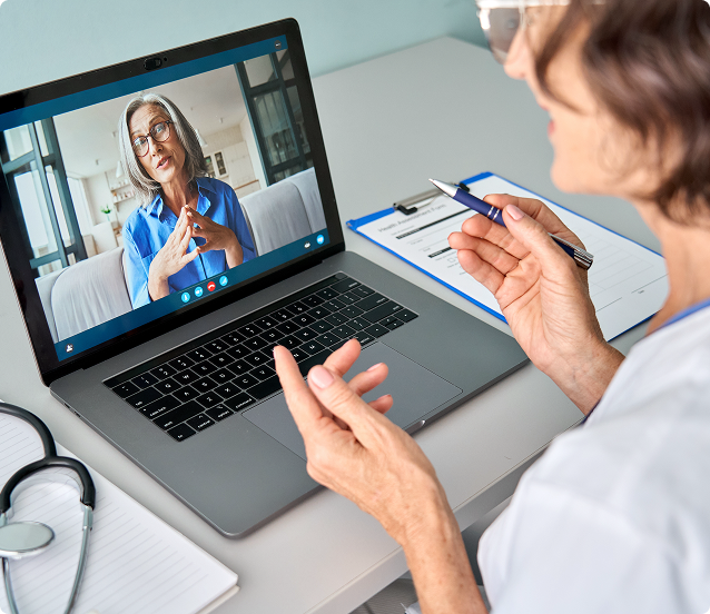 A healthcare provider in a white coat consults with a patient via video call on a laptop.