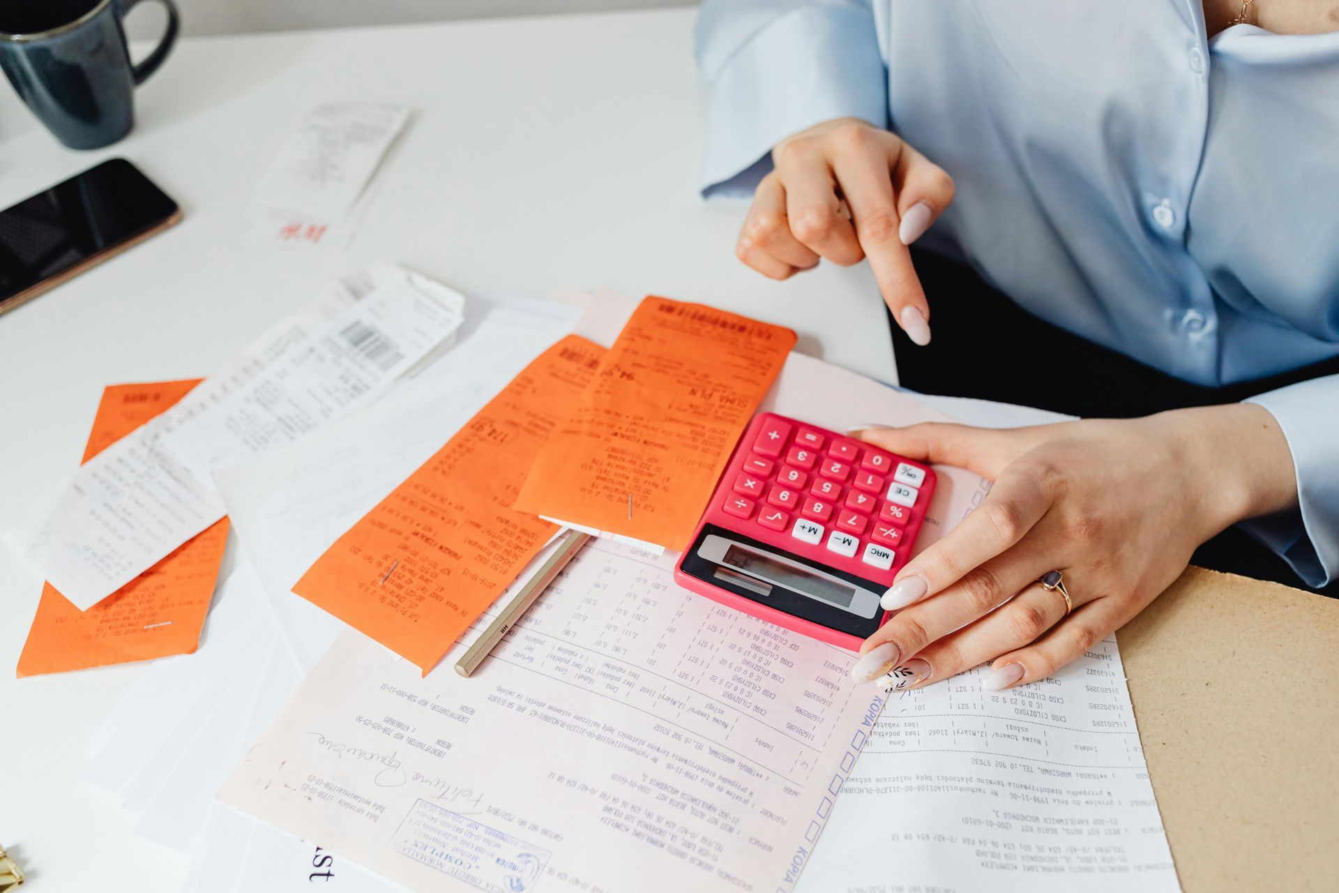 A woman is sitting at a table using a pink calculator.