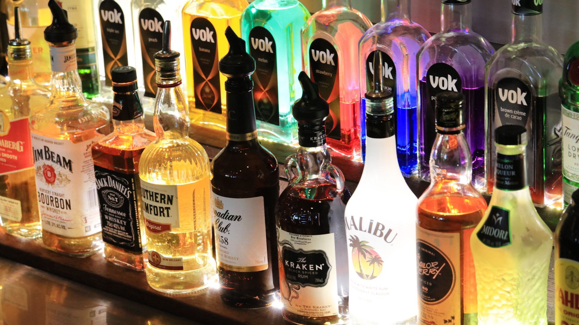 A row of bottles of liquor are lined up on a bar.