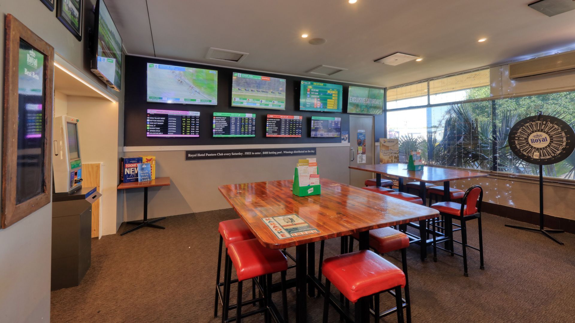 A room with tables and chairs and a lot of televisions on the wall.