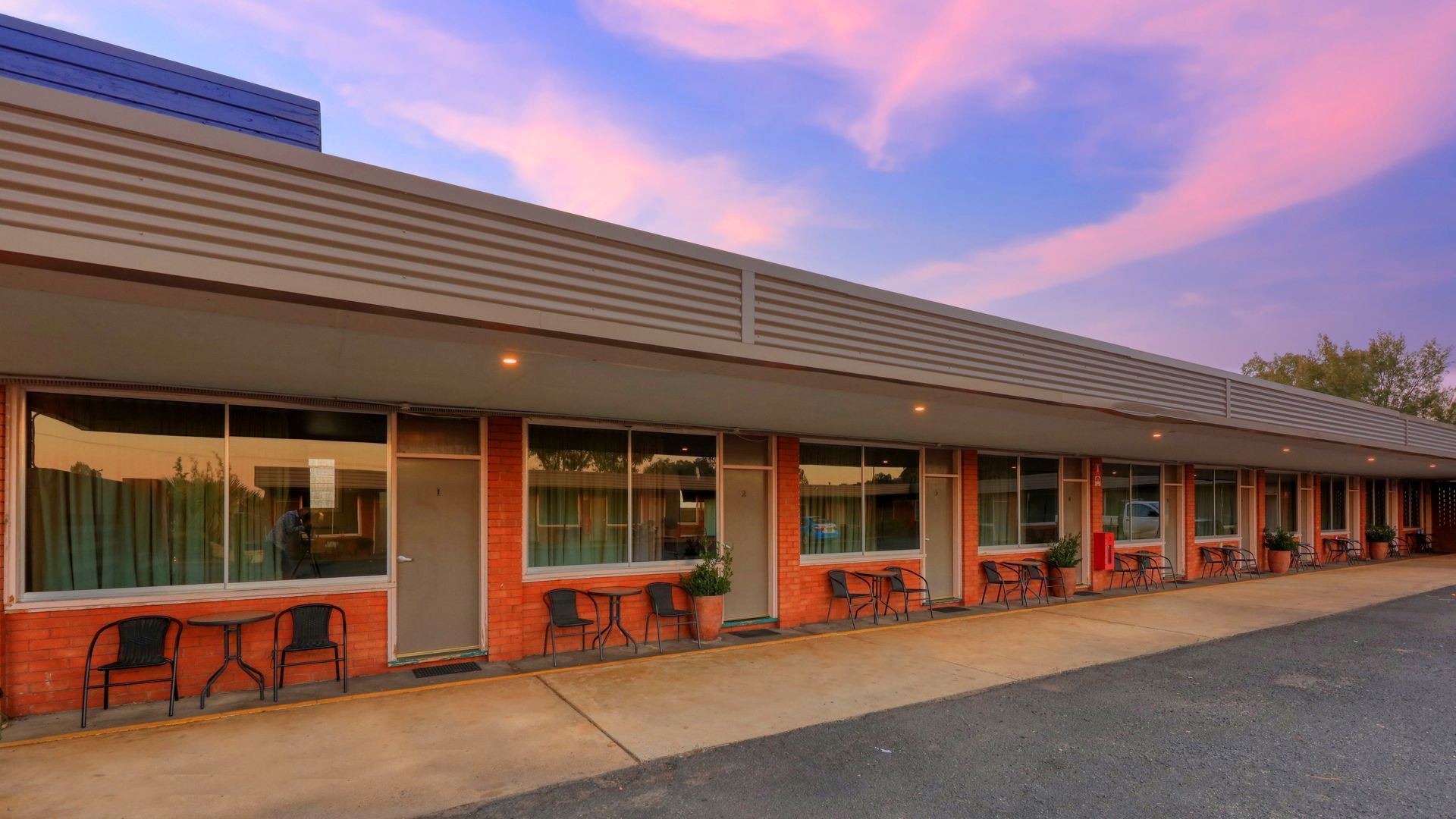 A motel with tables and chairs in front of it at sunset.