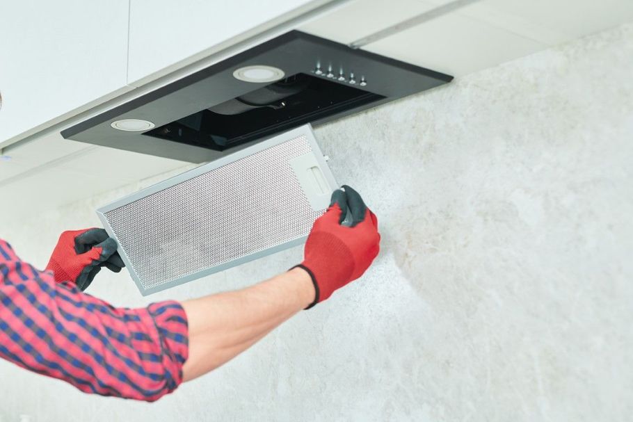 Person installing a white ceiling vent filter with red gloves using a ladder