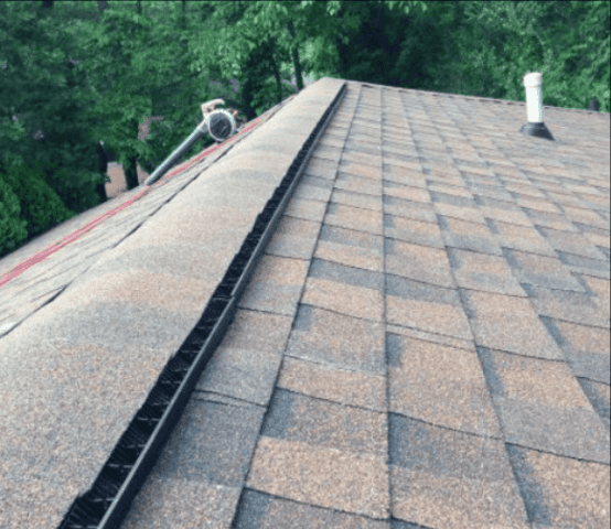 A brown shingled roof with a black trough-like structure along its ridge, trees in the background.