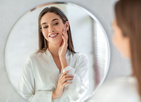 A woman is looking at her face in a mirror.