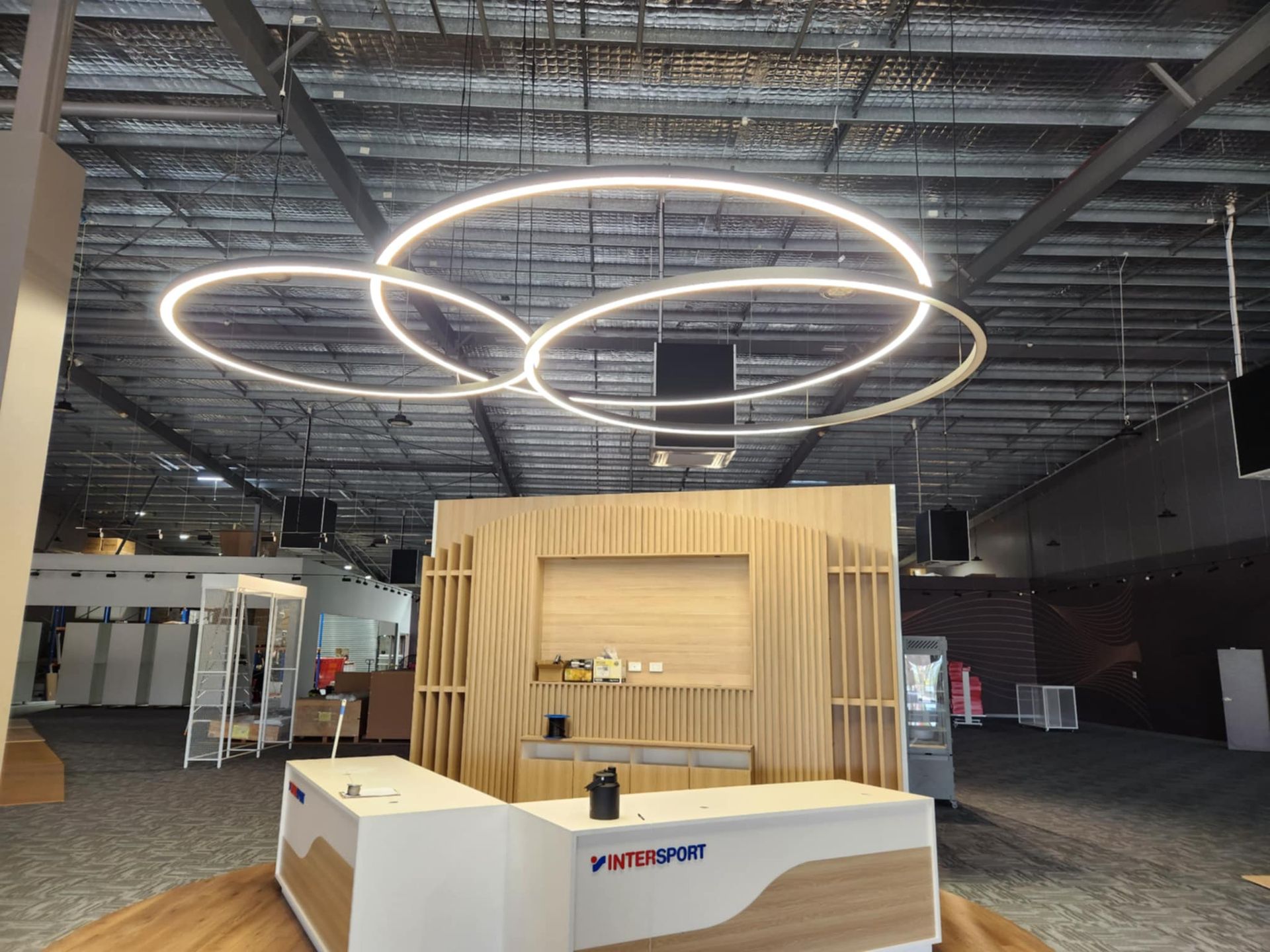 A modern reception area with a circular light fixture, a wooden backdrop, and a counter. — Watkins Electrical In Fraser Coast, QLD