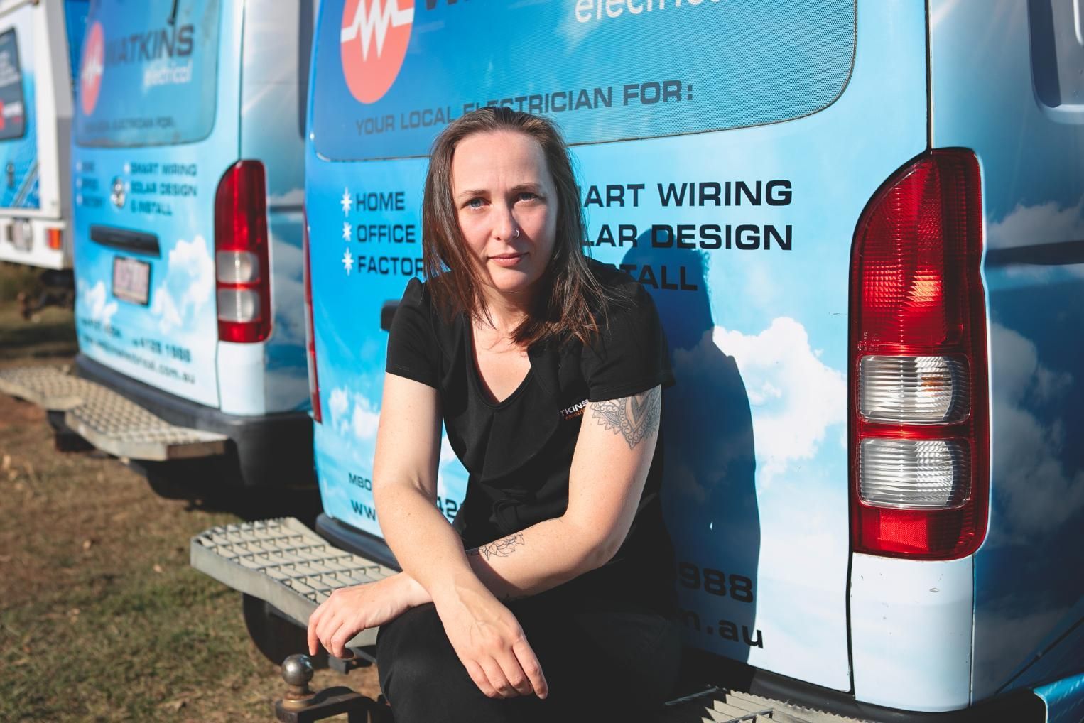 Woman sitting on the bumper of a blue van — Watkins Electrical In Pialba, QLD
