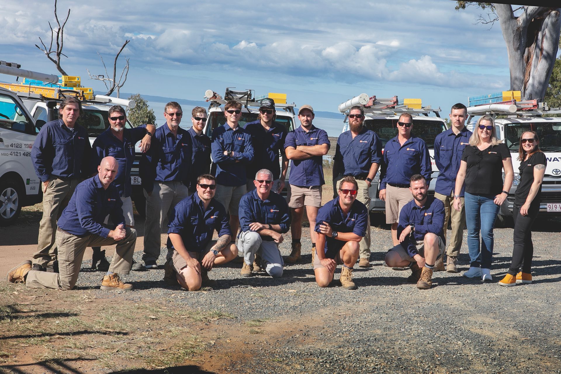 Group of people in uniform posing near work vehicles — Watkins Electrical In Pialba, QLD