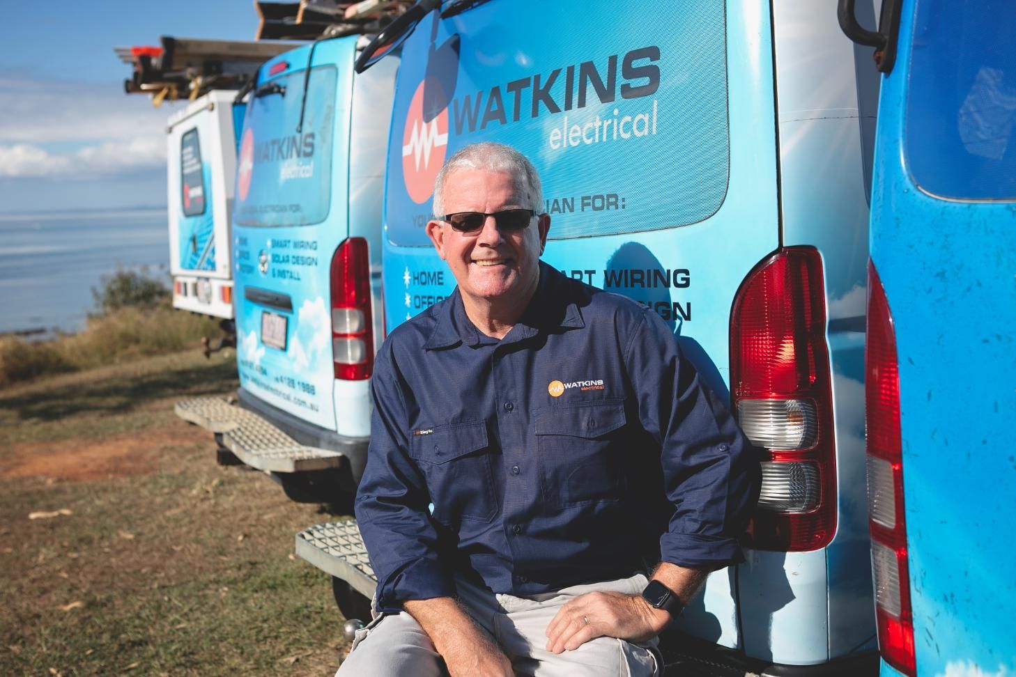 Man in blue shirt sits on a Watkins Electrical van, smiling — Watkins Electrical In Pialba, QLD