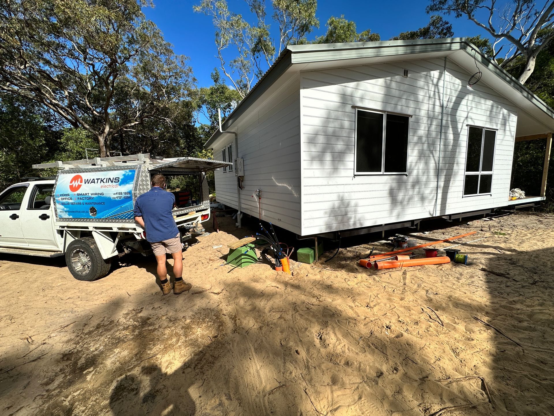 A man near a white house being built. A truck with a blue logo is parked nearby — Watkins Electrical In Pialba, QLD