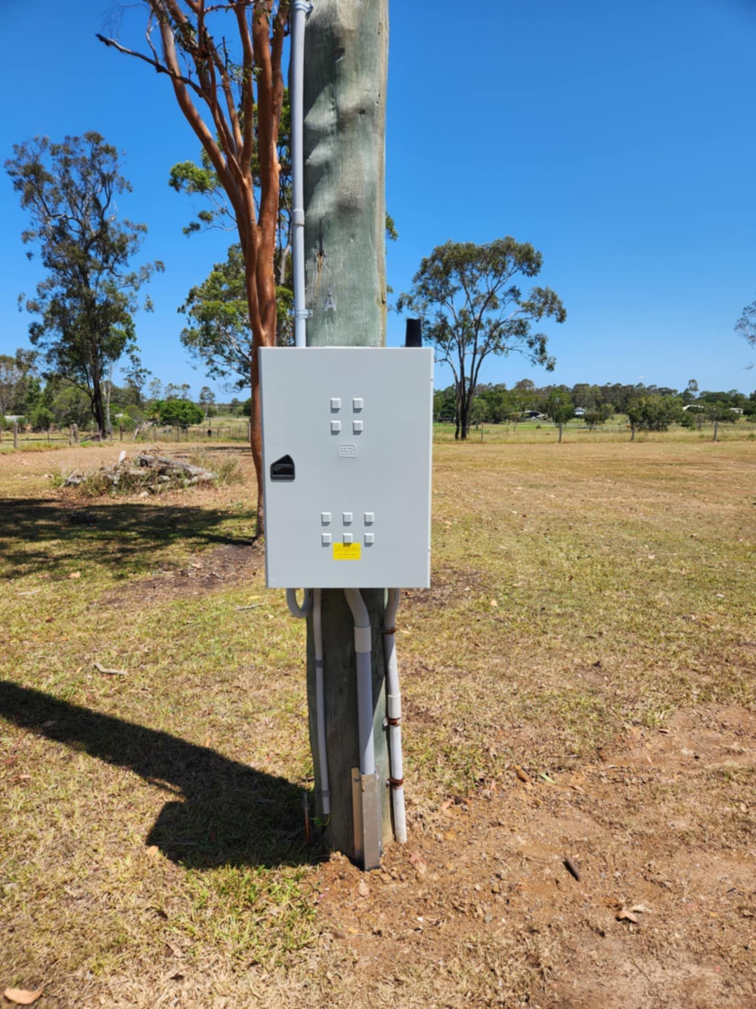 Gray electrical box mounted on a wooden utility pole, in a grassy field under a blue sky — Watkins Electrical In Pialba, QLD