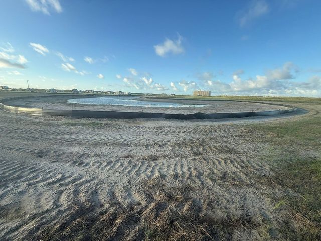 Wide sandy beach with rippled foreground and shallow tidal pools under a blue sky with scattered clouds.