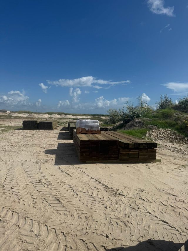 Sandy beach with stacked pallets and a clear blue sky over the shoreline.