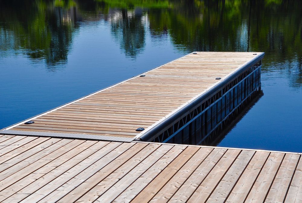 Wooden dock extending into calm blue water, with trees reflected in the background.