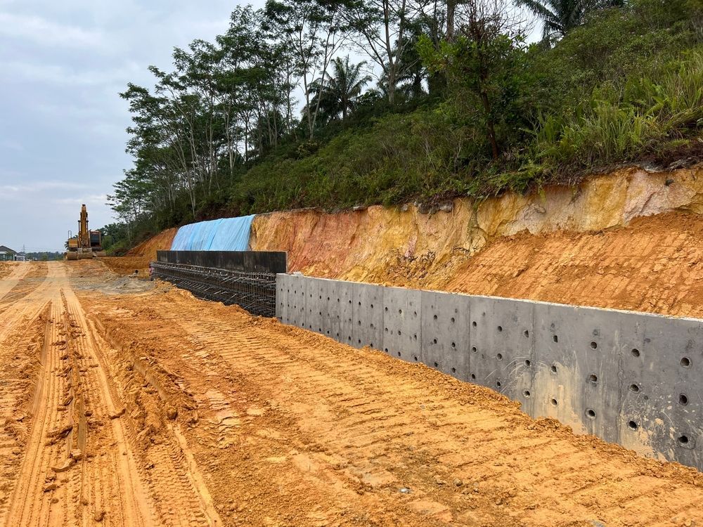 Roadside construction with concrete retaining wall beside a dirt road and hillside vegetation