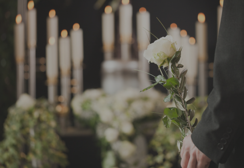 A person in black holding a white rose at a candlelit memorial with flowers in the background