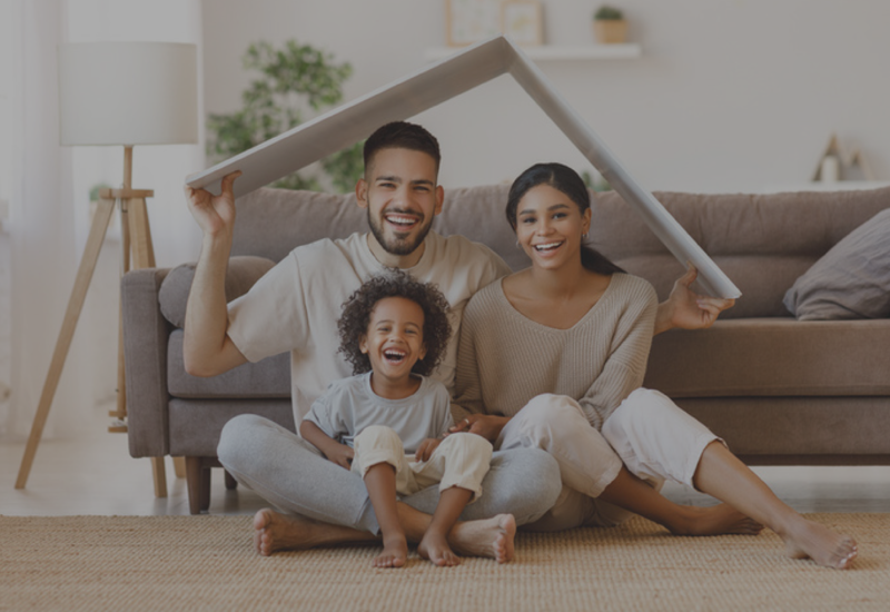 Smiling family sitting on a living room floor, holding a cardboard roof frame together