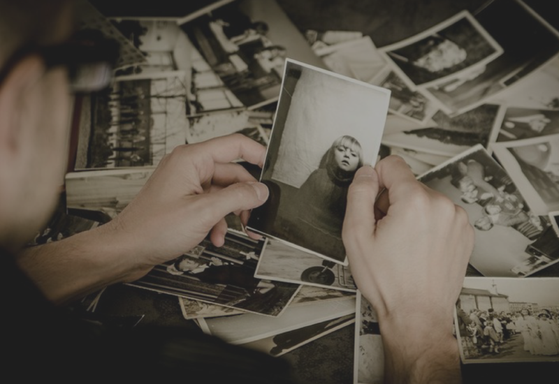 Hands sorting through a pile of black-and-white photographs on a table
