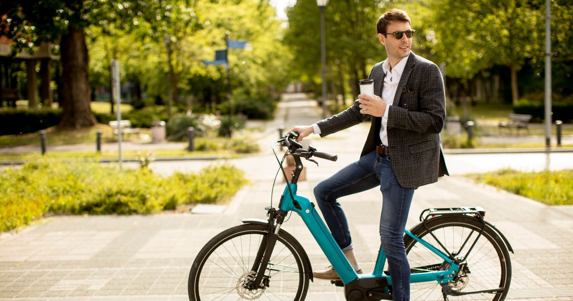 Een man rijdt op een elektrische fiets op de stoep terwijl hij een kop koffie vasthoudt.