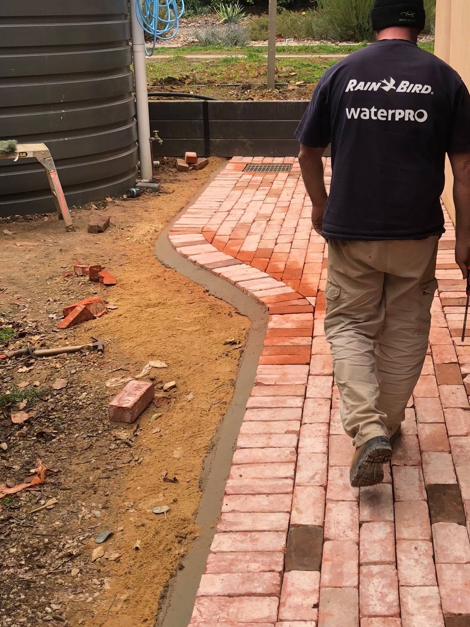 Worker walking on a curved brick path beside a water tank and dirt ground