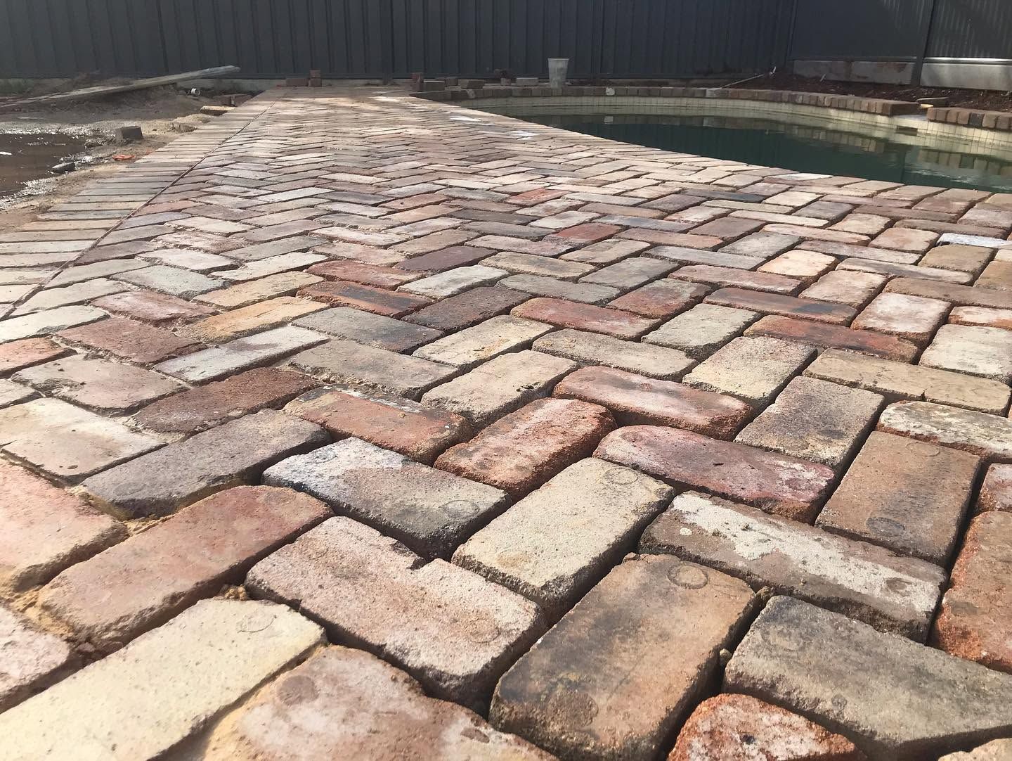 Brick-paved walkway with a wet sheen, bordered by dark fencing and water in the distance
