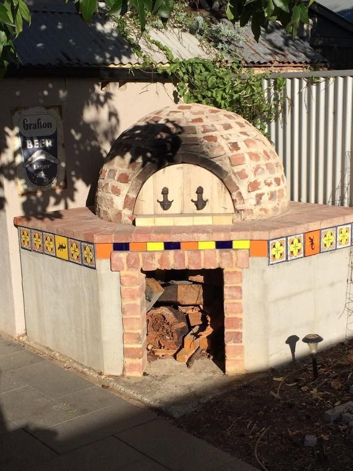 Outdoor brick pizza oven with domed top, decorative tile border, and an open firebox in a garden