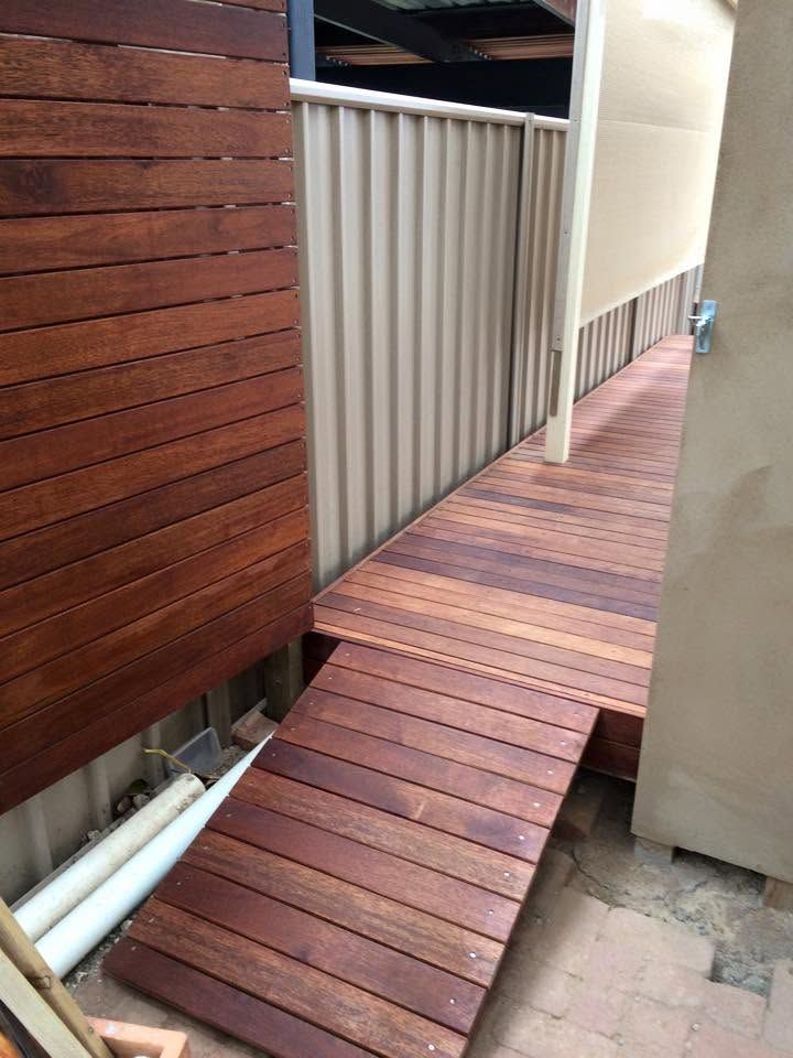 Narrow wooden ramp beside a corrugated metal fence in an outdoor walkway.