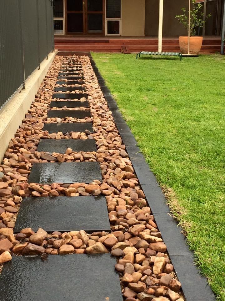 Stepping-stone walkway bordered by rocks beside a green lawn in a backyard garden