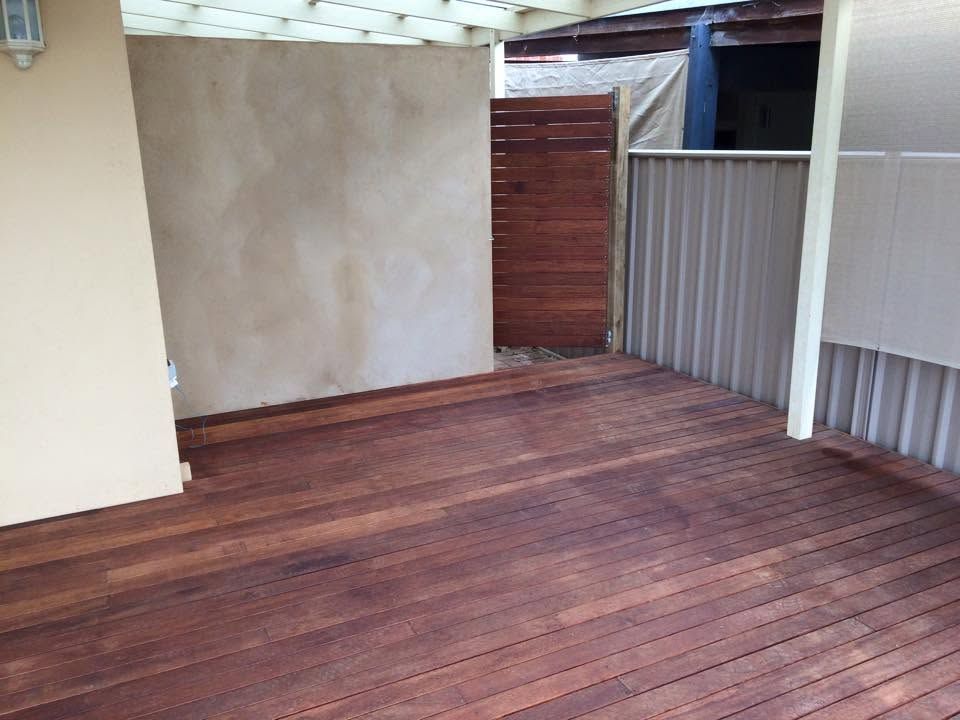 Empty covered patio with wooden deck and beige walls, opening to a small fenced area