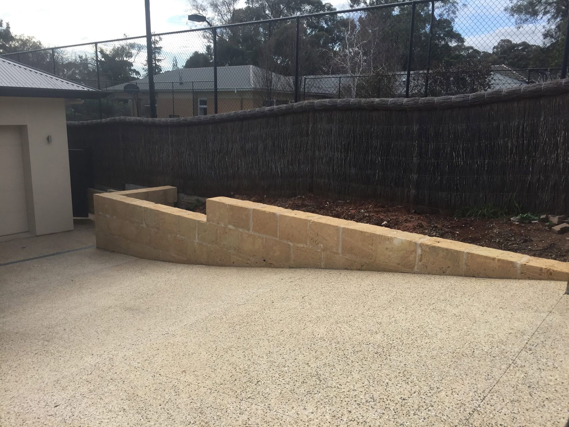 Concrete driveway with a tan retaining wall ramp beside a dark fence