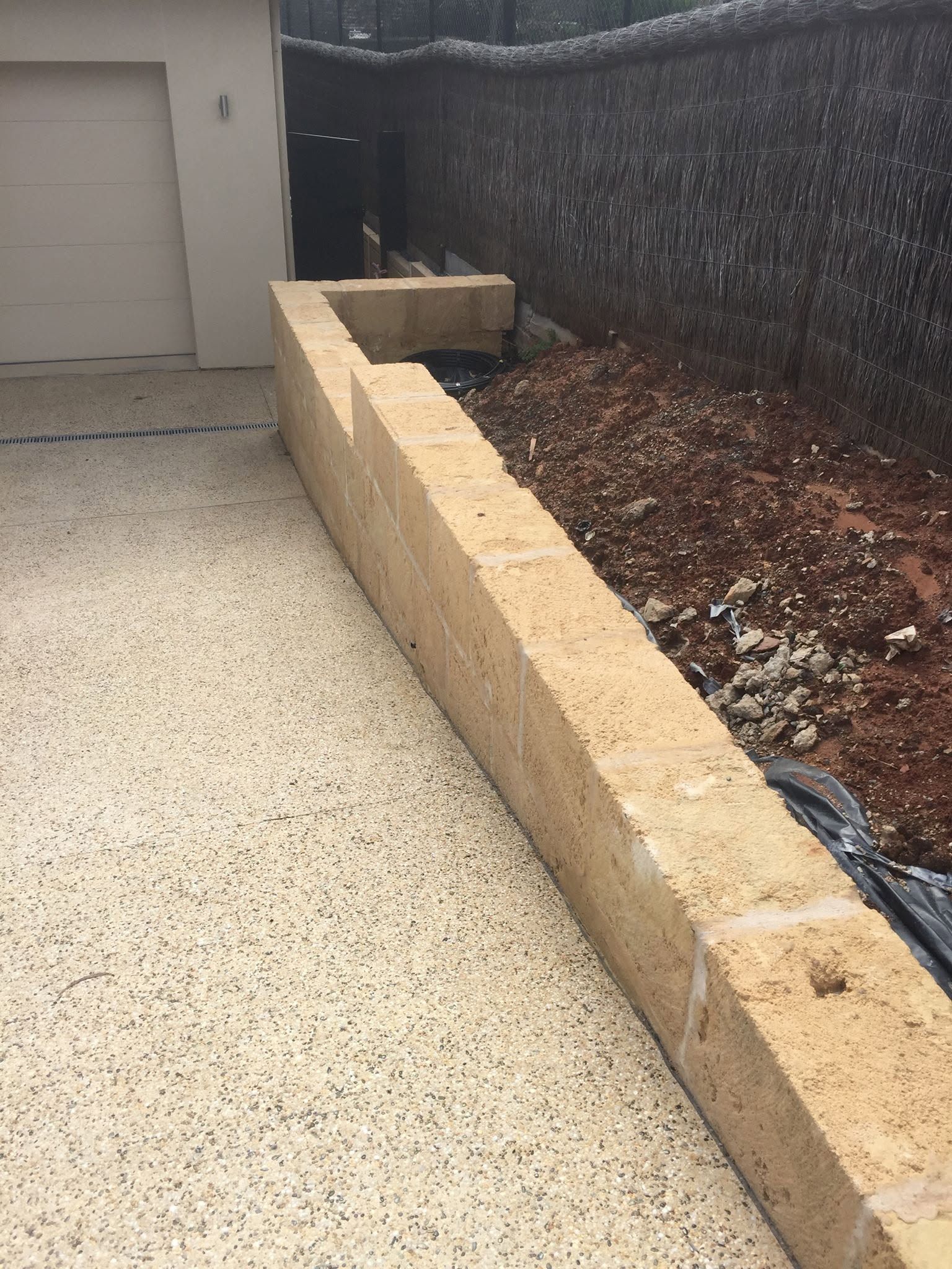 Concrete driveway beside a tan retaining wall and mulch bed next to a garage door