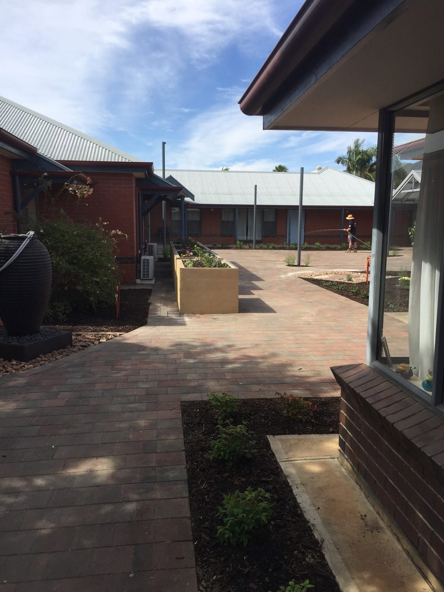 Courtyard with brick paving, a planter, and buildings under a sunny sky