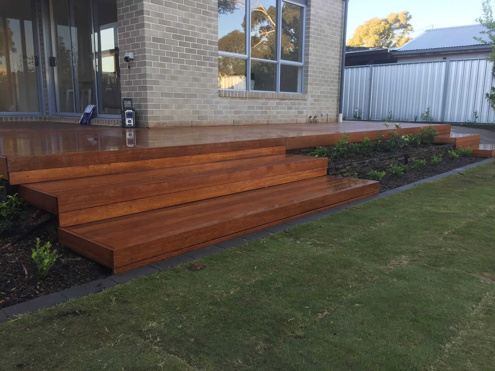 Wooden front porch steps beside a brick house and lawn, with garden beds along the walkway. Wooden front porch steps beside a brick house and lawn, with garden beds along the walkway.