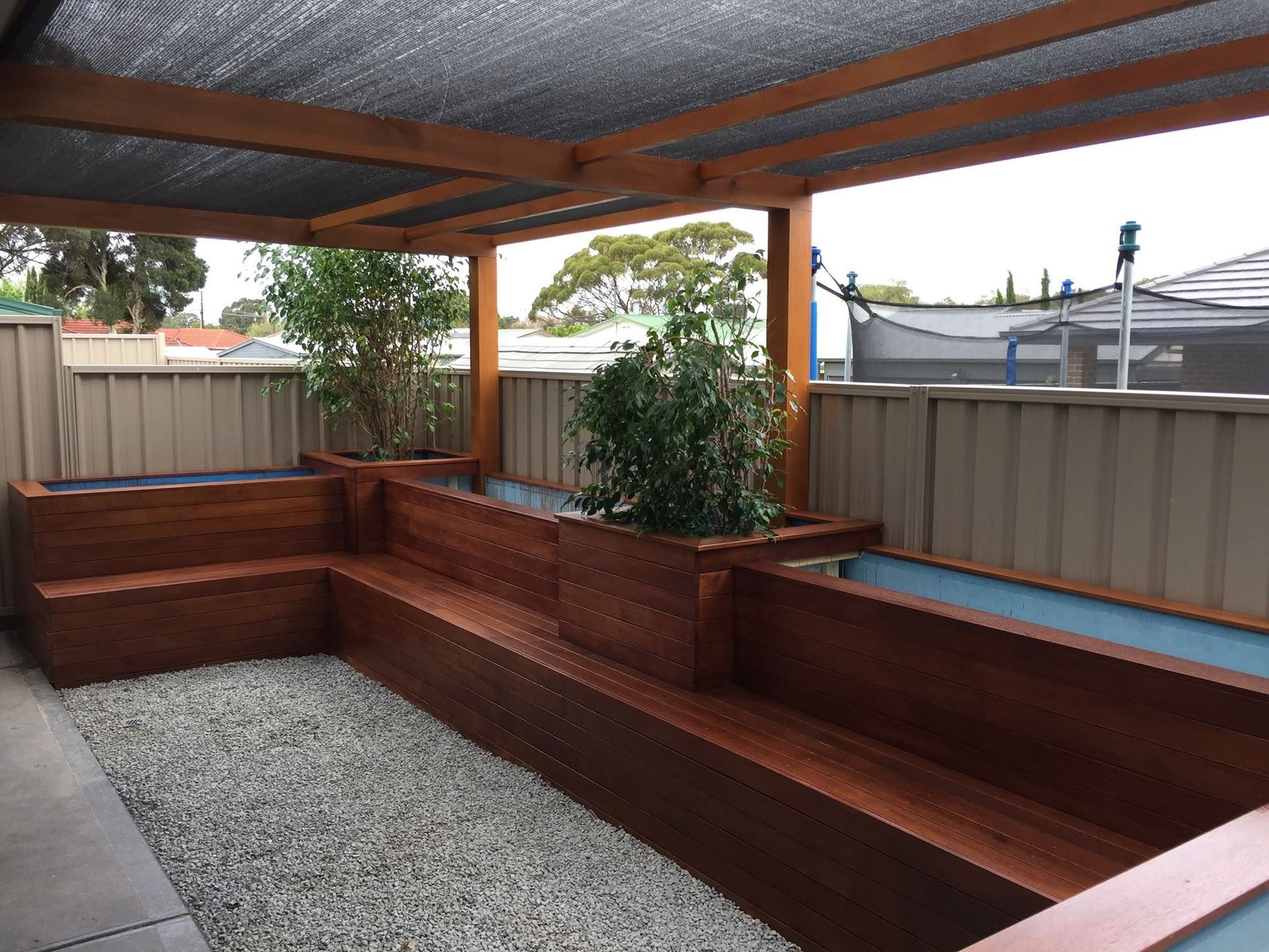 Wooden backyard deck with built-in benches, gravel center, and pergola roof beside a privacy fence