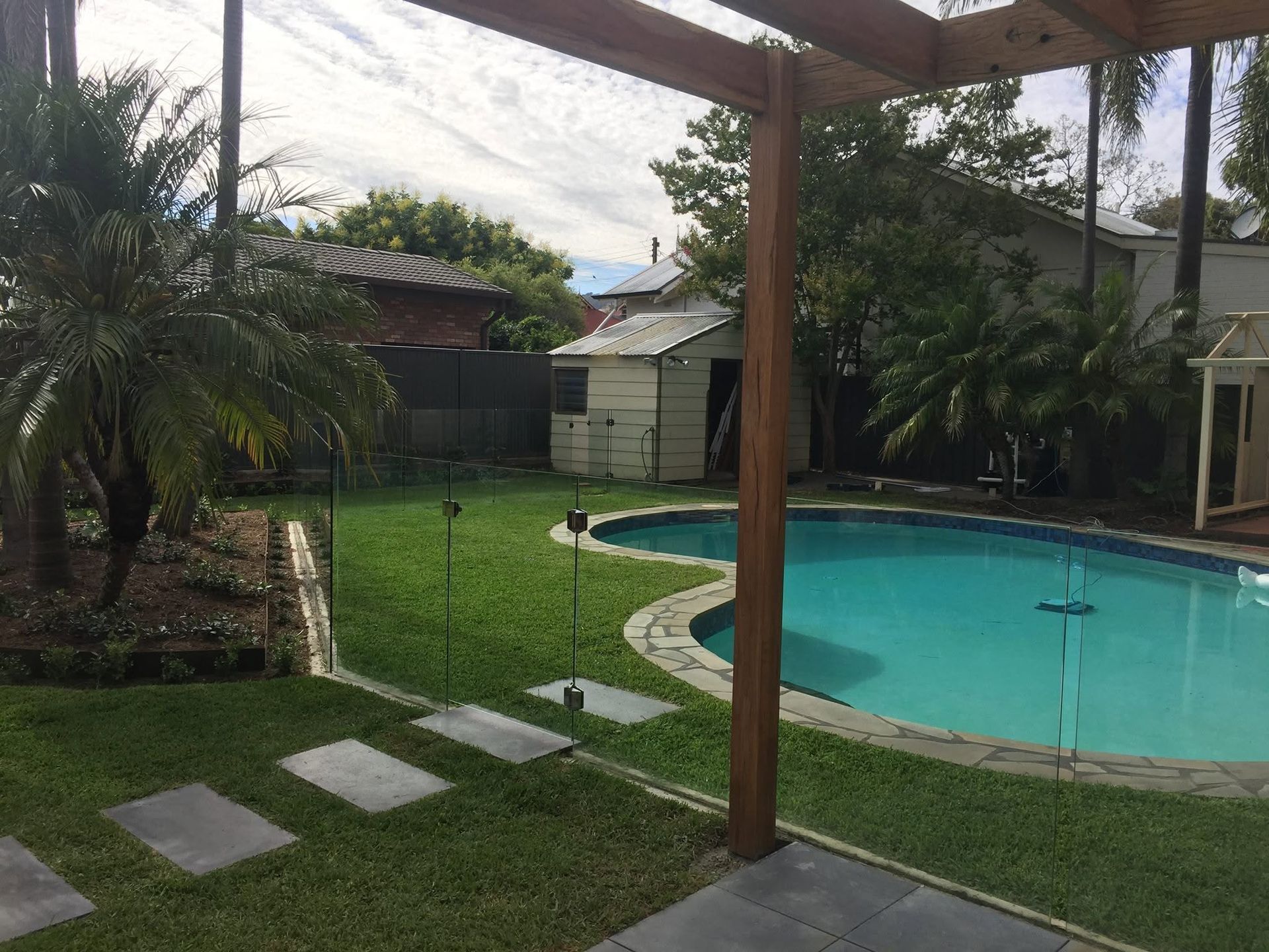 Backyard pool with green lawn, stone path, and wooden pergola overlooking a fenced yard. Backyard pool with green lawn, stone path, and wooden pergola overlooking a fenced yard.