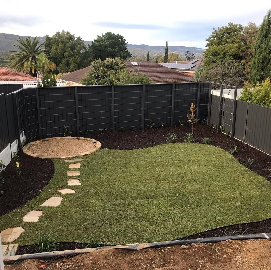 Small backyard with green lawn, stepping stones, dark fence, and landscaped border plants. Small backyard with green lawn, stepping stones, dark fence, and landscaped border plants.