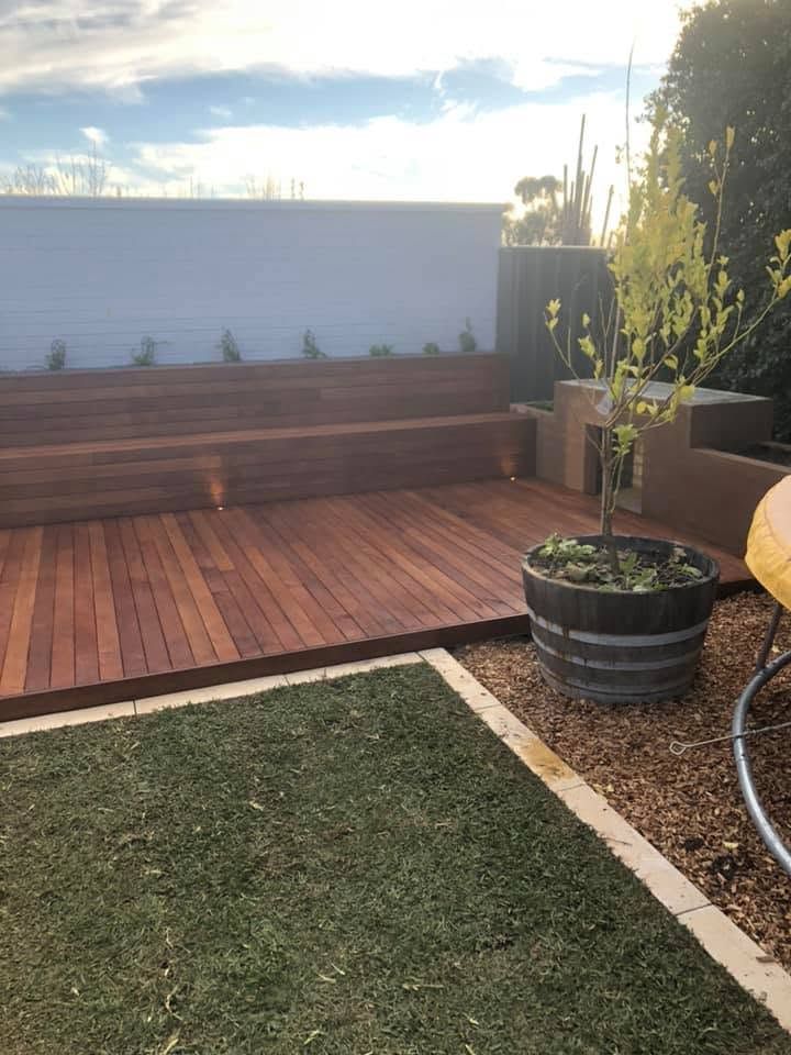 Backyard patio with wooden deck, bench seating, potted plants, and a grassy lawn in warm sunlight Backyard patio with wooden deck, bench seating, potted plants, and a grassy lawn in warm sunlight