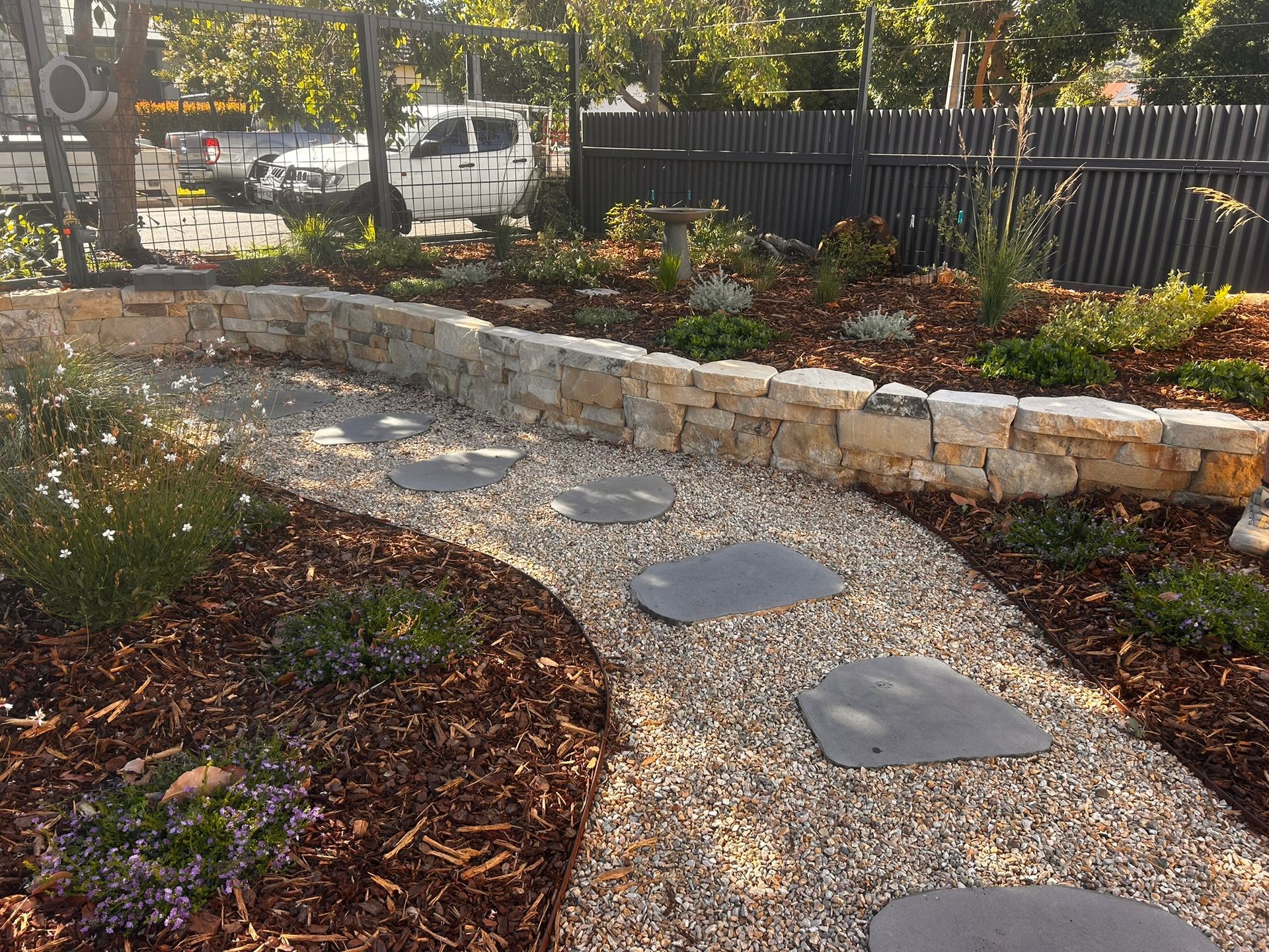 Curved gravel garden path with stepping stones beside a raised stone planter and flowers