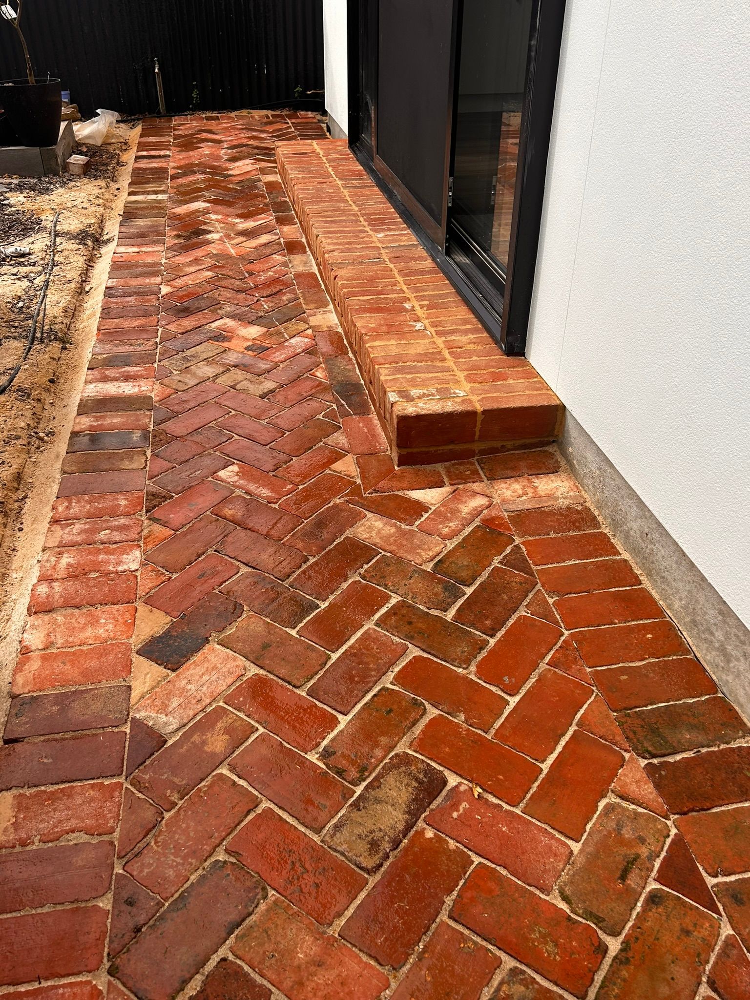 Curved terracotta brick walkway beside a stone house and garden shrubs